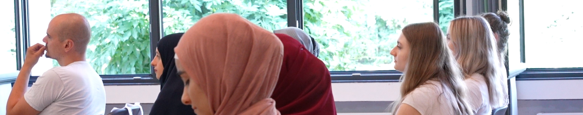Ein seitliches Bild, das mehrere Teilnehmerinnen und Teilnehmer eines Seminars in einer Reihe zeigt, darunter auch einige Frauen mit und ohne Kopftuch.