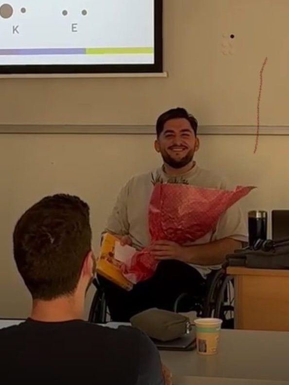 Zu sehen ist Ahmet von Dima e.V. Er hat nach seinem Vortrag ein Geschenk überreicht bekommen und lächelt in die Kamera.